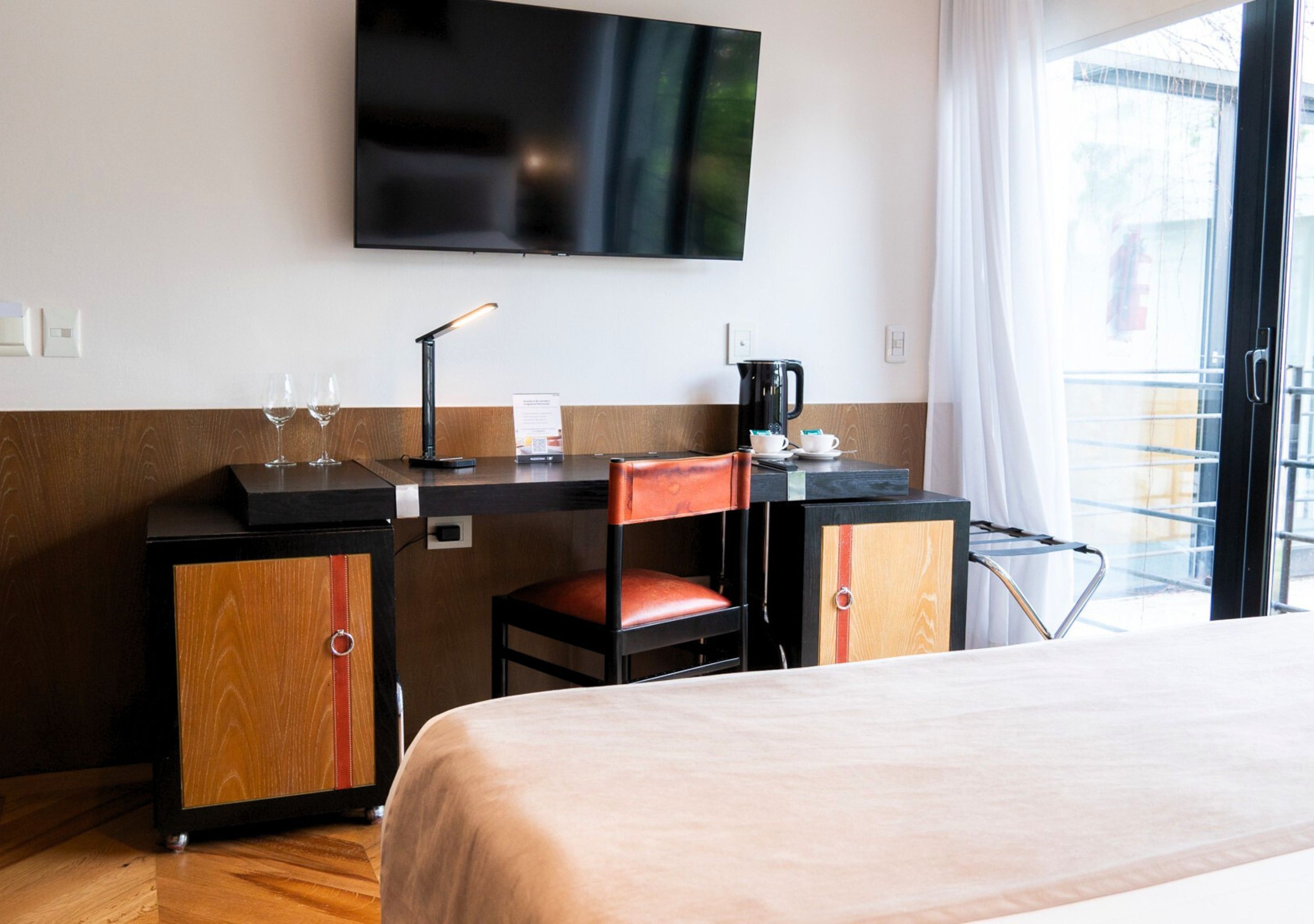 A hotel room with a bed, a desk with a chair, a television, and a window with a view of the outside.
