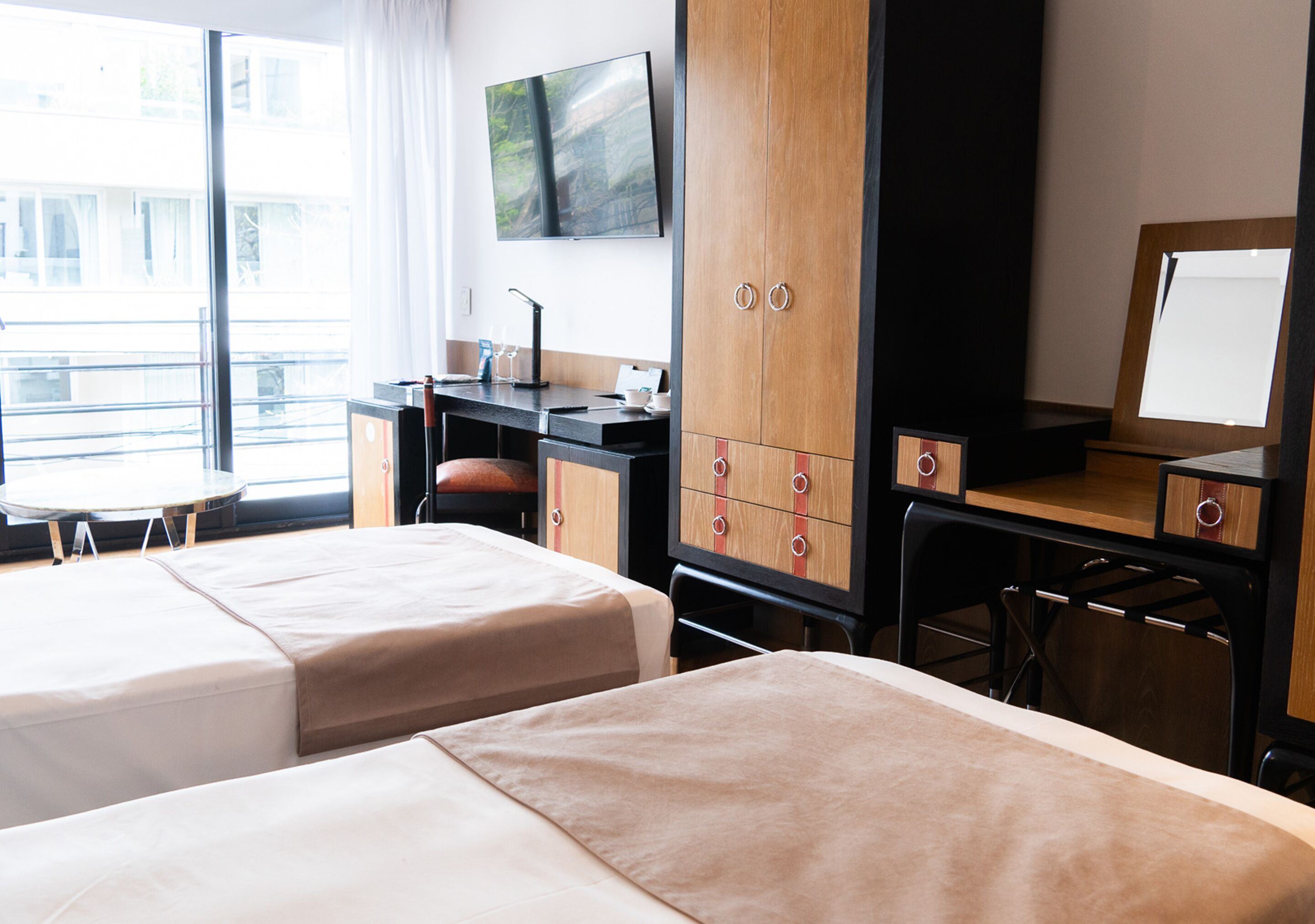 Une chambre d’hôtel avec deux lits, un bureau, une chaise, une télévision et une fenêtre donnant sur l’extérieur.