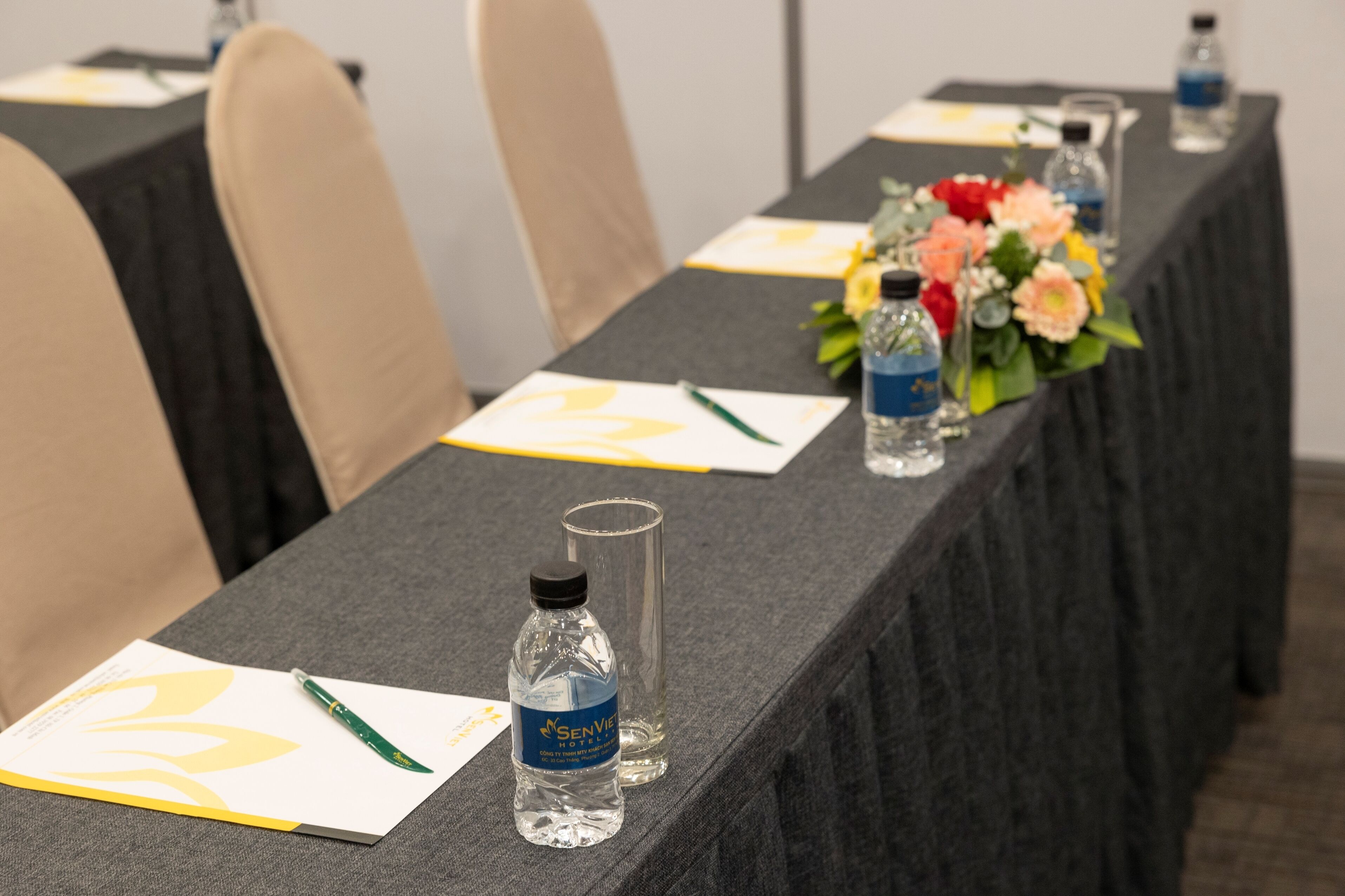 Una mesa de conferencias con botellas de agua, bolígrafos y un arreglo floral.