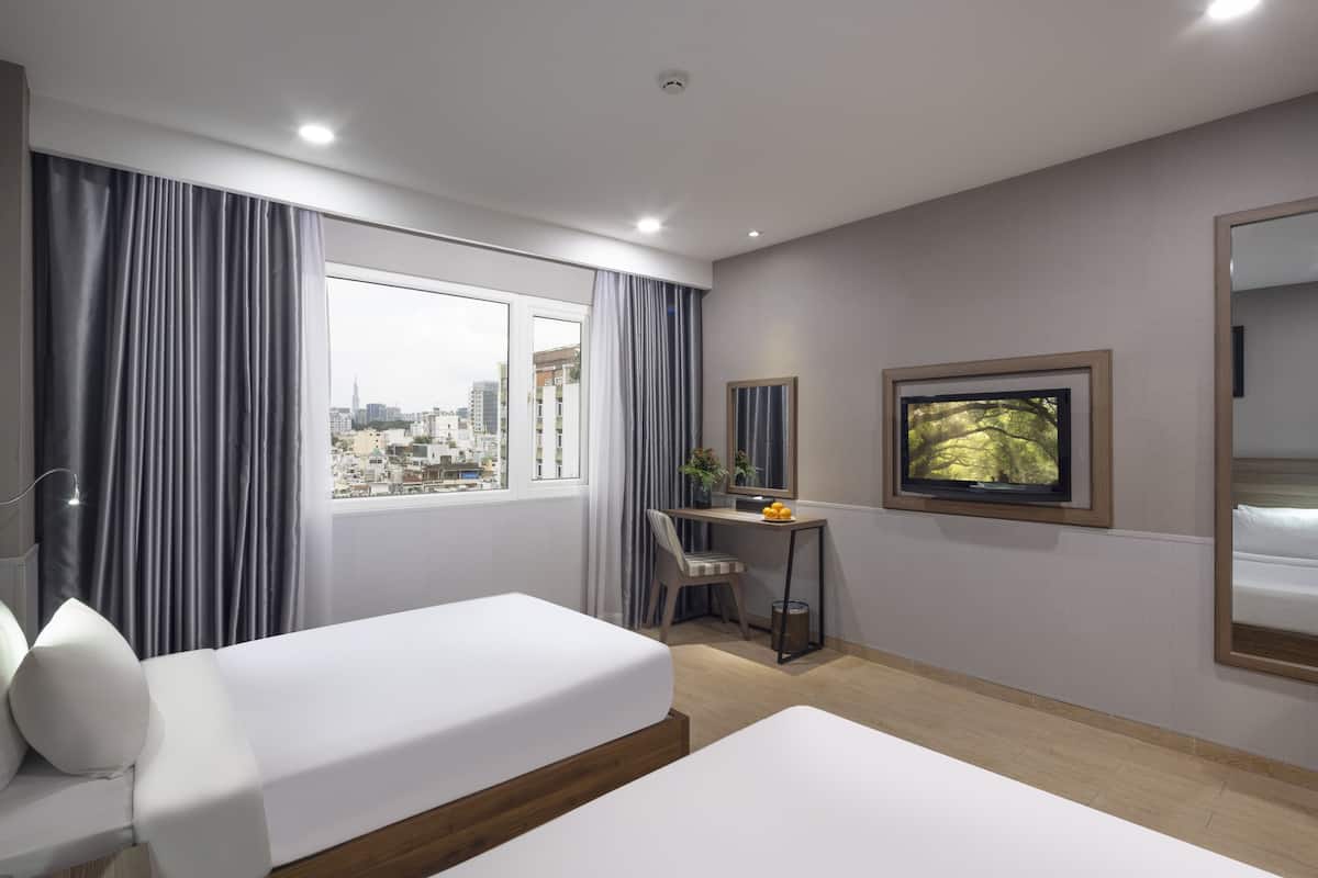 Une chambre d’hôtel avec deux lits simples, un bureau avec une chaise, une télévision et une grande fenêtre avec des rideaux.
