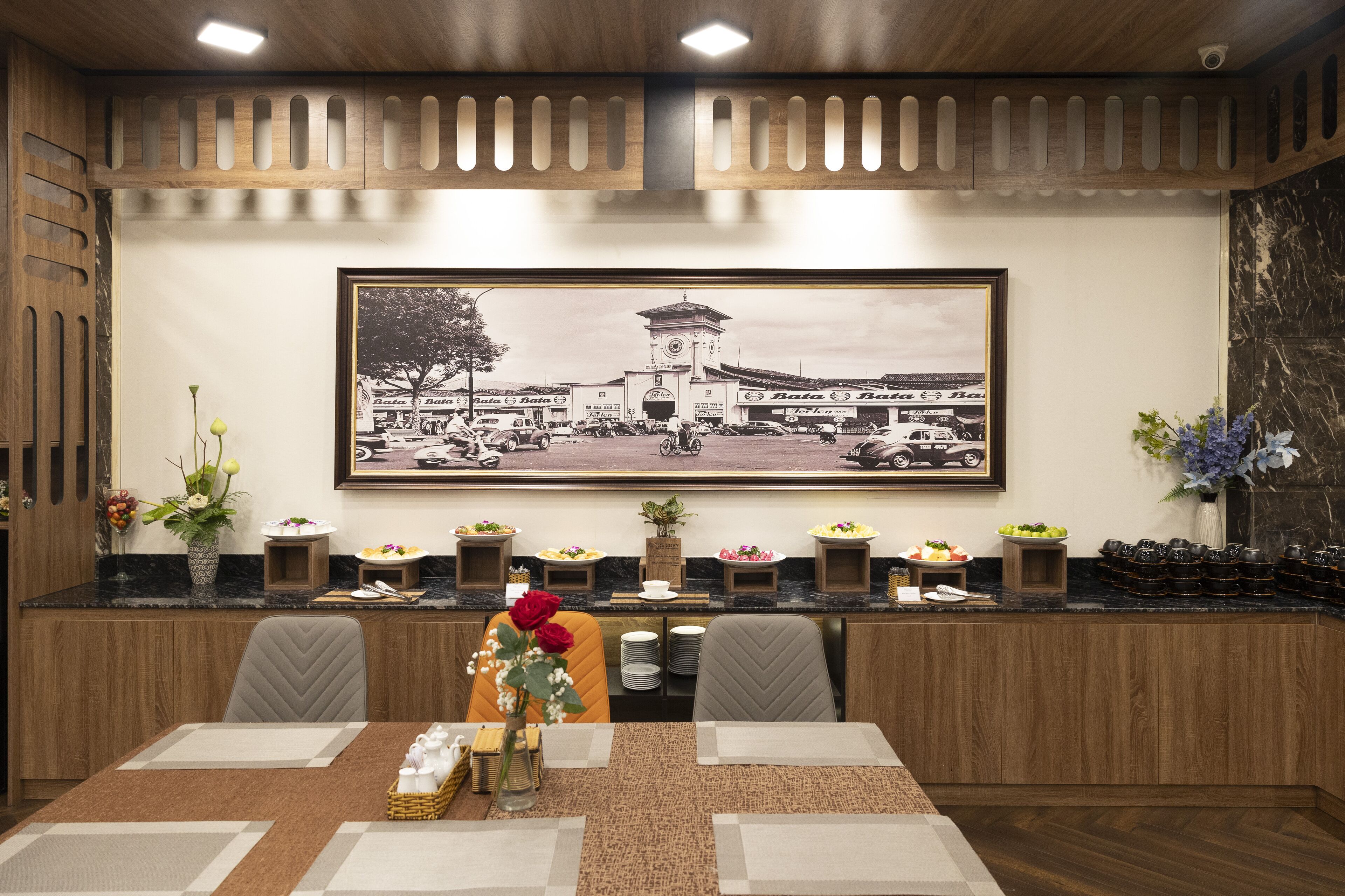 A dining area with a long table, chairs, a framed black and white photo on the wall, and a buffet setup with various dishes.