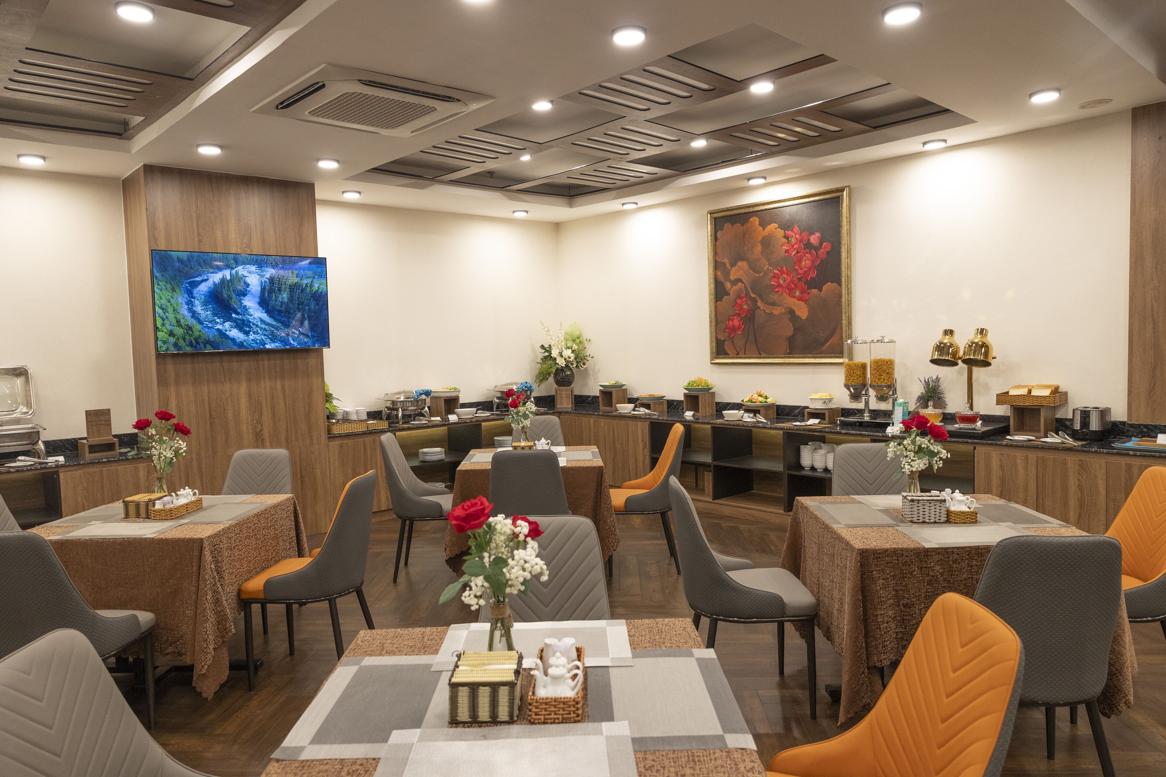 Un vestíbulo de hotel con varias mesas de comedor, sillas, una mesa de recepción y una gran pantalla de televisión.