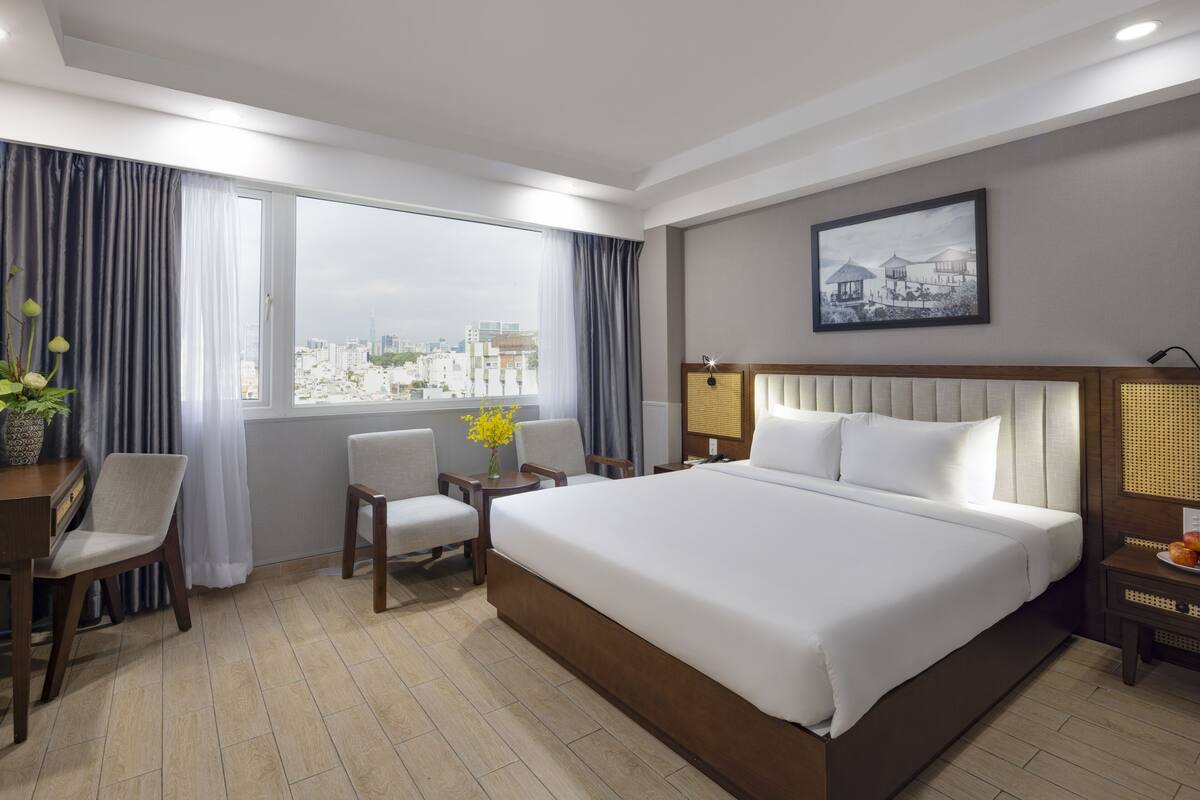 Une chambre d’hôtel avec un grand lit, deux fauteuils, un bureau, une lampe et une vue sur la ville.