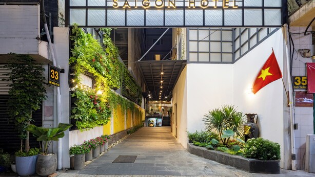 The entrance to Vet Lotus Saigon Hotel with a modern design, featuring a glass facade, a flag, and a well-lit pathway.