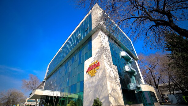 A modern hotel with a prominent logo, large windows, and a well-maintained lawn. - Astra (Almaty)