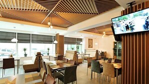 A modern dining area with wooden ceiling panels, a flat-screen TV mounted on the wall, and a view of the city through large windows. - Astra (Almaty)