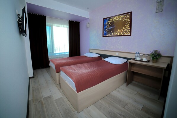 A hotel room with two beds, a desk, a TV, and a window with curtains.