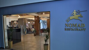 The entrance to Nomad Restaurant with a glass door, potted plants, and a sign featuring a running figure and a deer. - Astra (Almaty)