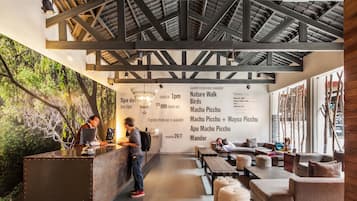 Un espace d’accueil doté d’un plafond en bois rustique, d’un comptoir de réception et d’un coin salon avec des canapés et des poufs.
