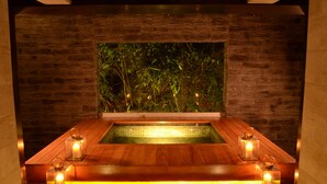 A spa area with a wooden bench, two candles, and a large window with a view of greenery. - El MaPi Hotel by Inkaterra (Machu Picchu)