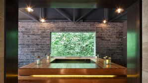 A modern spa room with a wooden floor, a large window with a view of greenery, and a built-in hot tub. - El MaPi Hotel by Inkaterra (Machu Picchu)