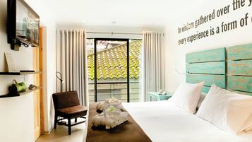 Habitación de hotel con cama, una silla, televisor, ventana con cortinas y una pared con una cita.
