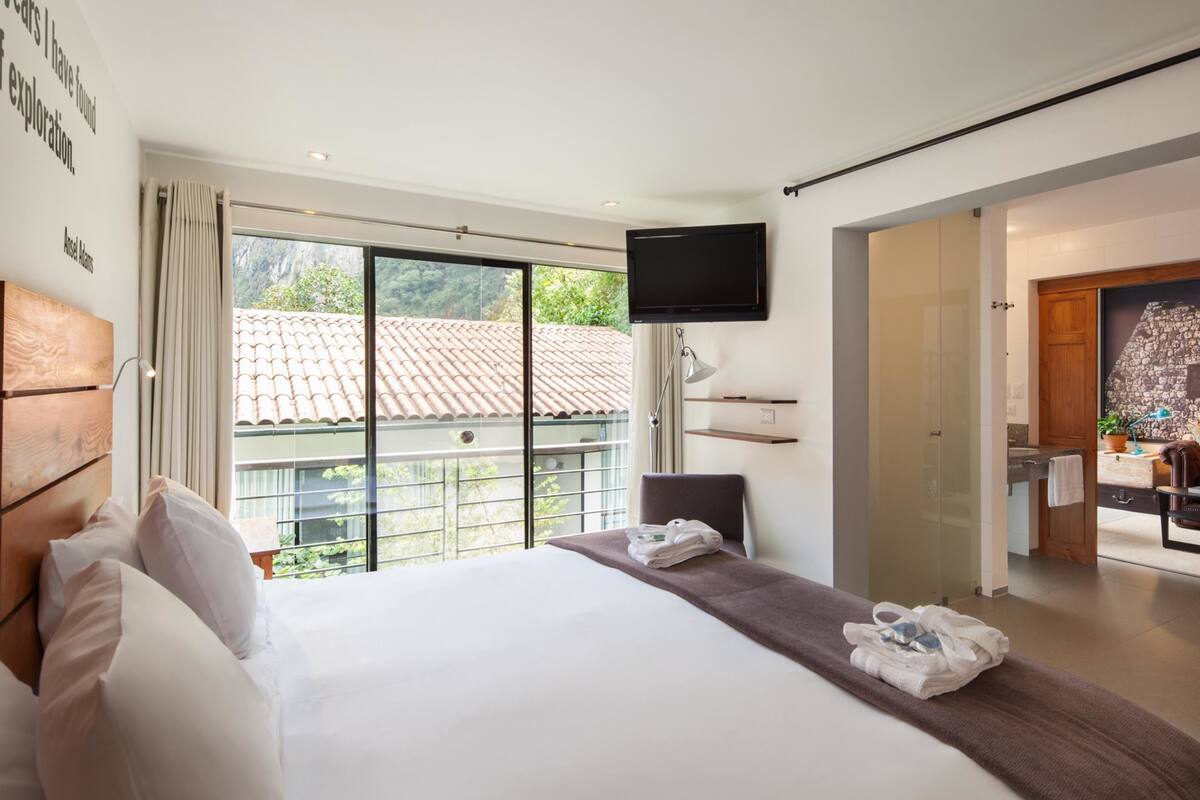 A modern hotel room with a large bed, a TV mounted on the wall, and a balcony with a view of the city.