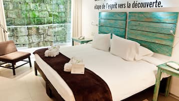 A hotel room with a large bed, a wooden headboard, a stone wall, a window, and a brown bench.
