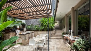 An outdoor dining area with stone walls, white chairs, and a chef preparing food. - El MaPi Hotel by Inkaterra (Machu Picchu)