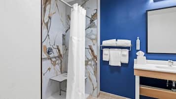 A bathroom with a marble wall, a shower curtain, a sink with a mirror, and neatly arranged towels.