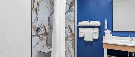 A bathroom with a marble wall, a shower curtain, a sink with a mirror, and neatly arranged towels.