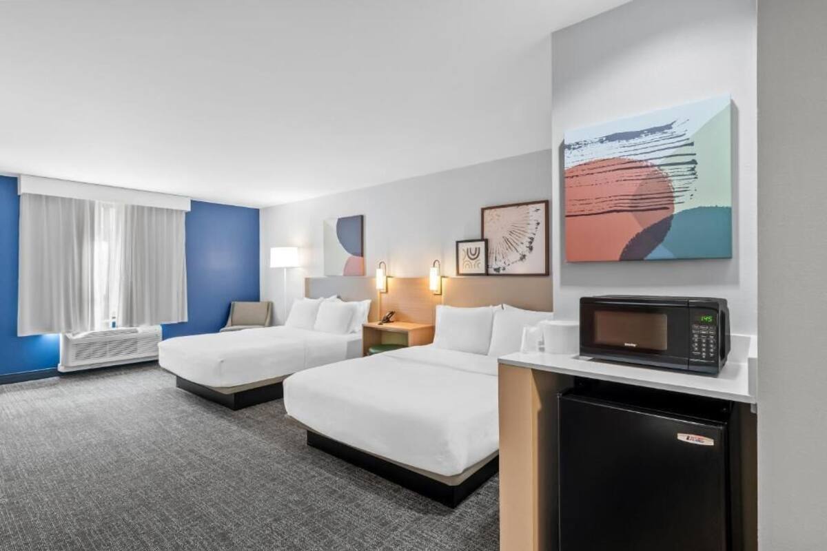 Habitación de hotel con dos camas, microondas, refrigerador pequeño, escritorio, lámpara y obras de arte en la pared.