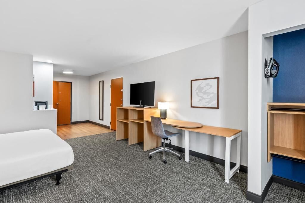 Une chambre d’hôtel avec un lit, un bureau, une chaise et un téléviseur fixé au mur.