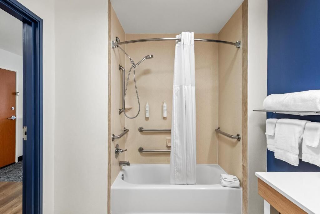 A bathroom with a bathtub, shower, and handrails.
