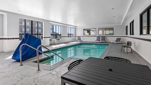 Un área de piscina interior moderna con vista despejada, una zona de estar cubierta y una mesa con sillas.