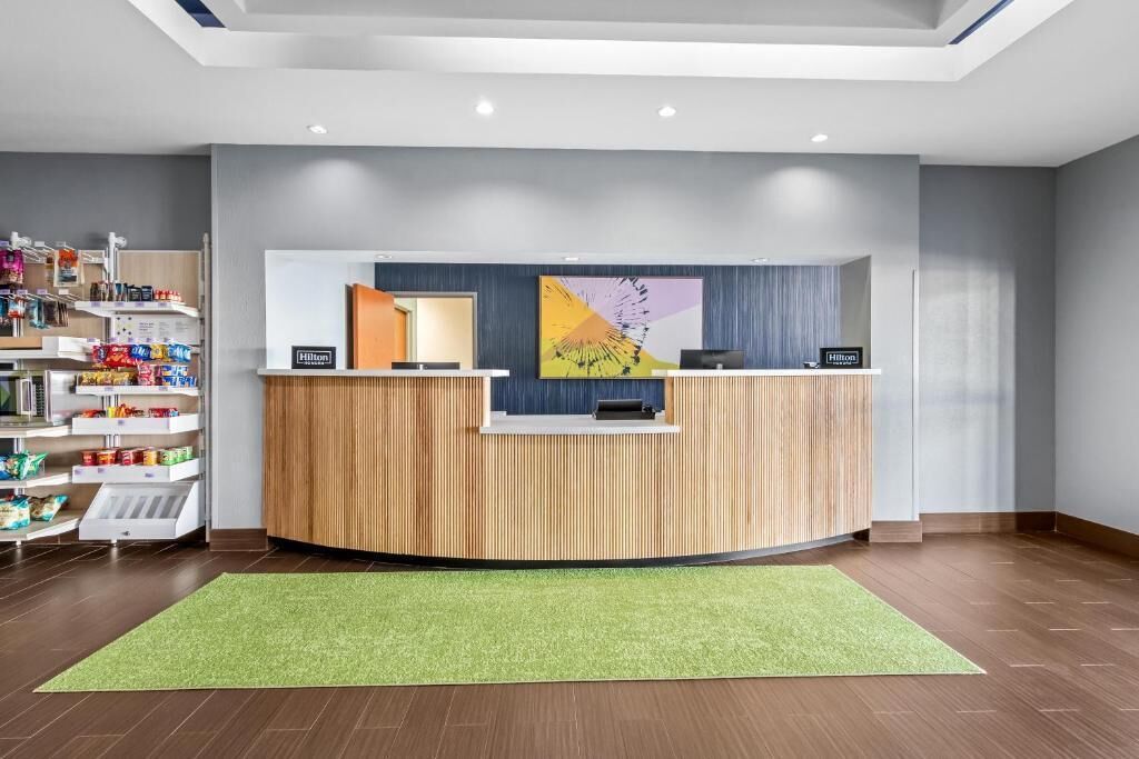 A hotel reception desk with a green carpet, wooden paneling, and a large abstract painting.