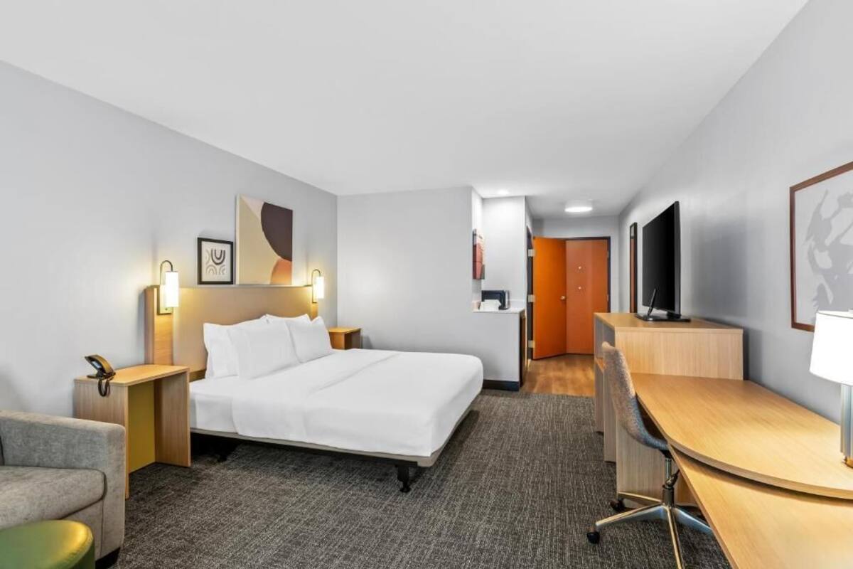 Una habitación de hotel con cama, escritorio, silla, mesita de noche, lámpara y televisor.