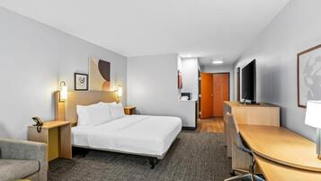 A hotel room with a bed, desk, chair, bedside table, lamp, and a television.