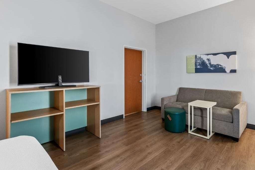Een kamer met een televisie op een houten bureau, een bank, een klein tafeltje en een deur.