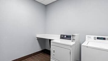 A laundry room with a white wall, a shelf, and two white Whirlpool washers.