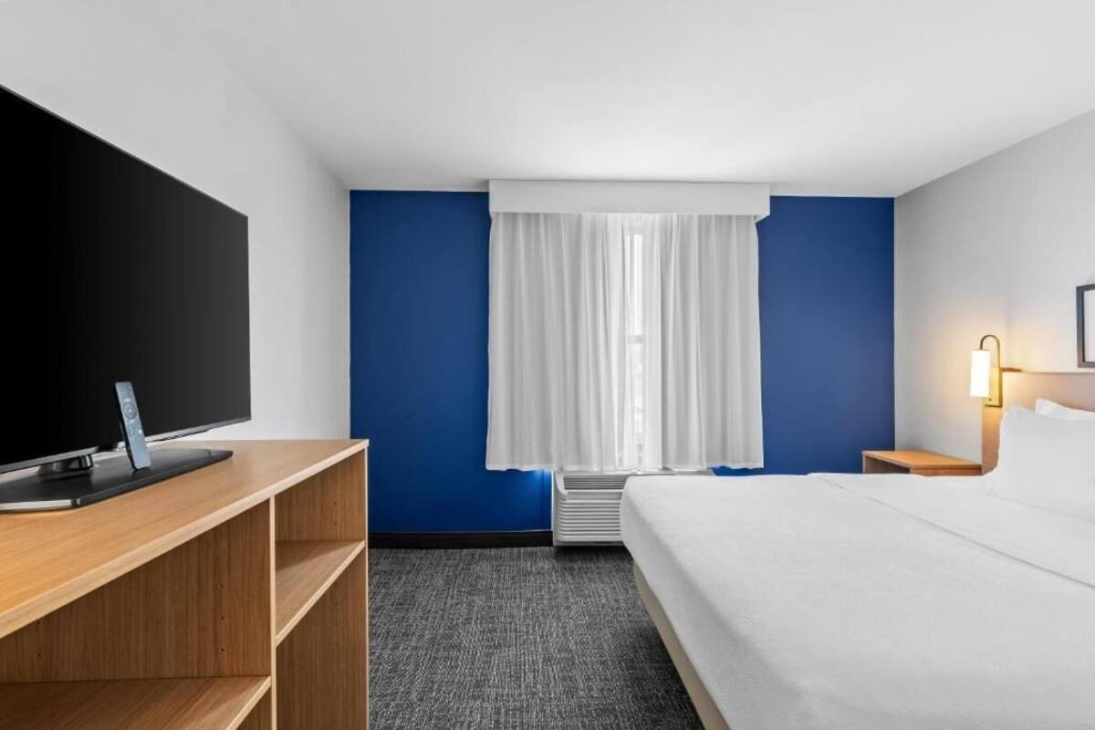 Una habitación de hotel con cama, televisión, escritorio y ventana con cortinas.