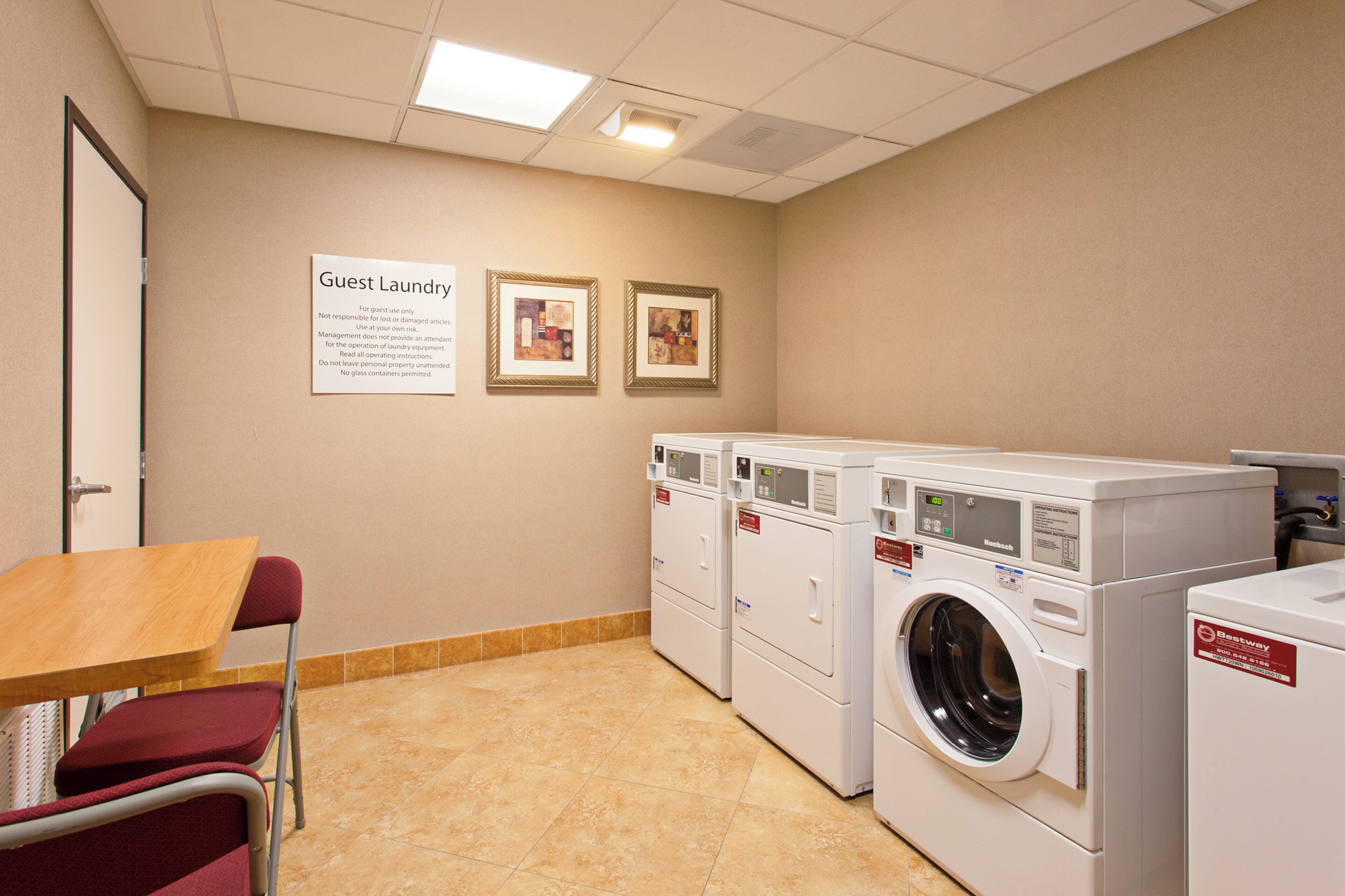 A laundry room with multiple washing machines, a table, chairs, and two framed pictures on the wall.