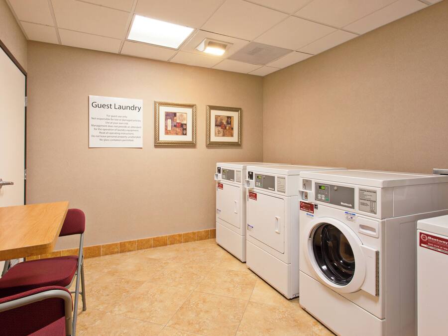 A laundry room with multiple washing machines, a table, chairs, and two framed pictures on the wall.