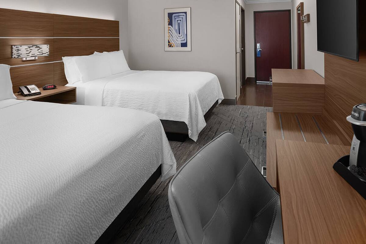 Une chambre d’hôtel avec deux lits, un bureau, une chaise, un téléviseur à écran plat et une porte.