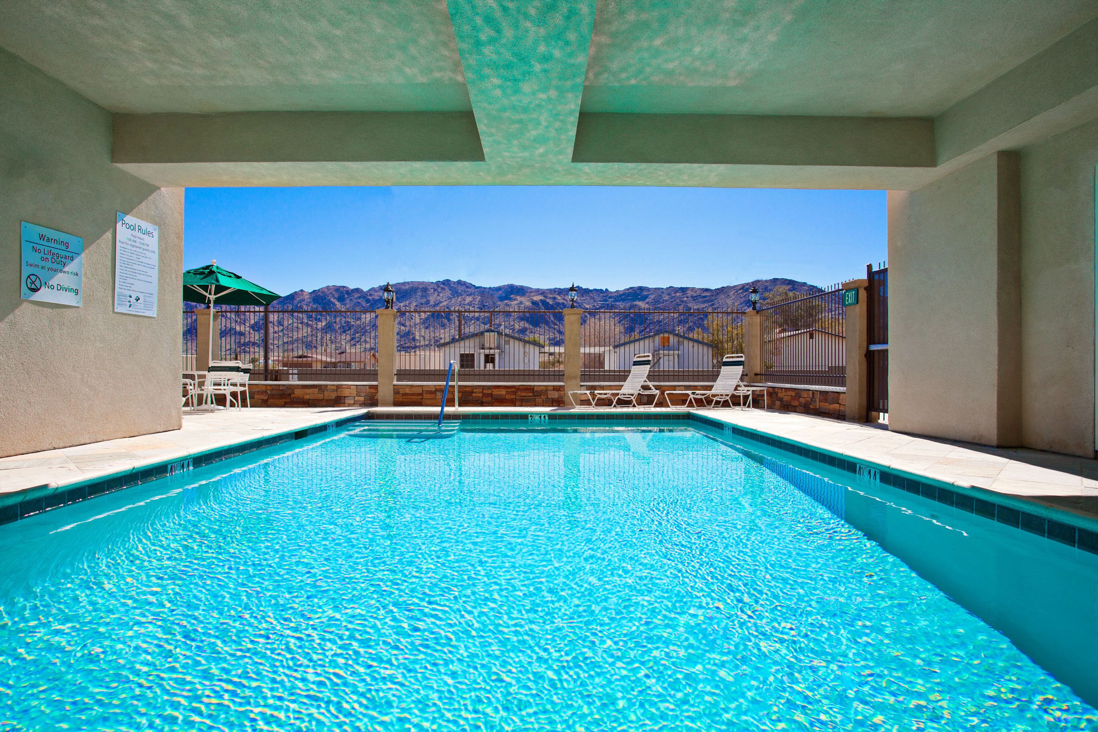 A swimming pool with a view of mountains in the background, surrounded by a fence and lounge chairs.