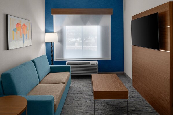 Una camera d'hotel moderna con una parete blu a contrasto, un divano, un tavolo di legno, una televisione a schermo piatto e una finestra con persiane.