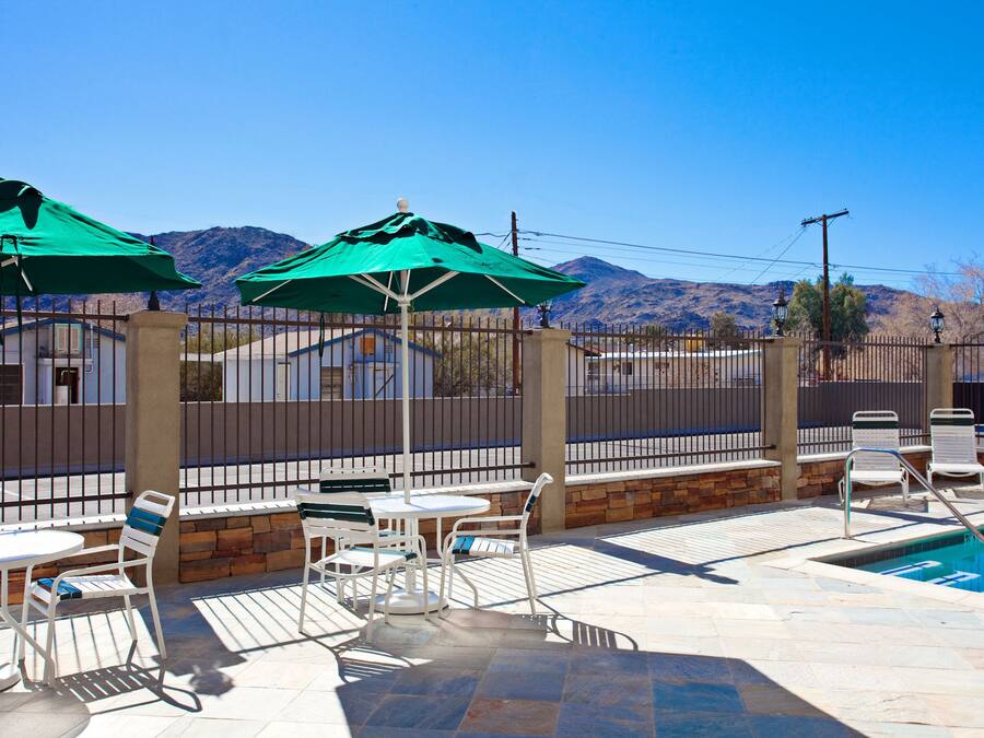 A poolside area with outdoor seating and umbrellas, surrounded by a fence and mountains in the background.