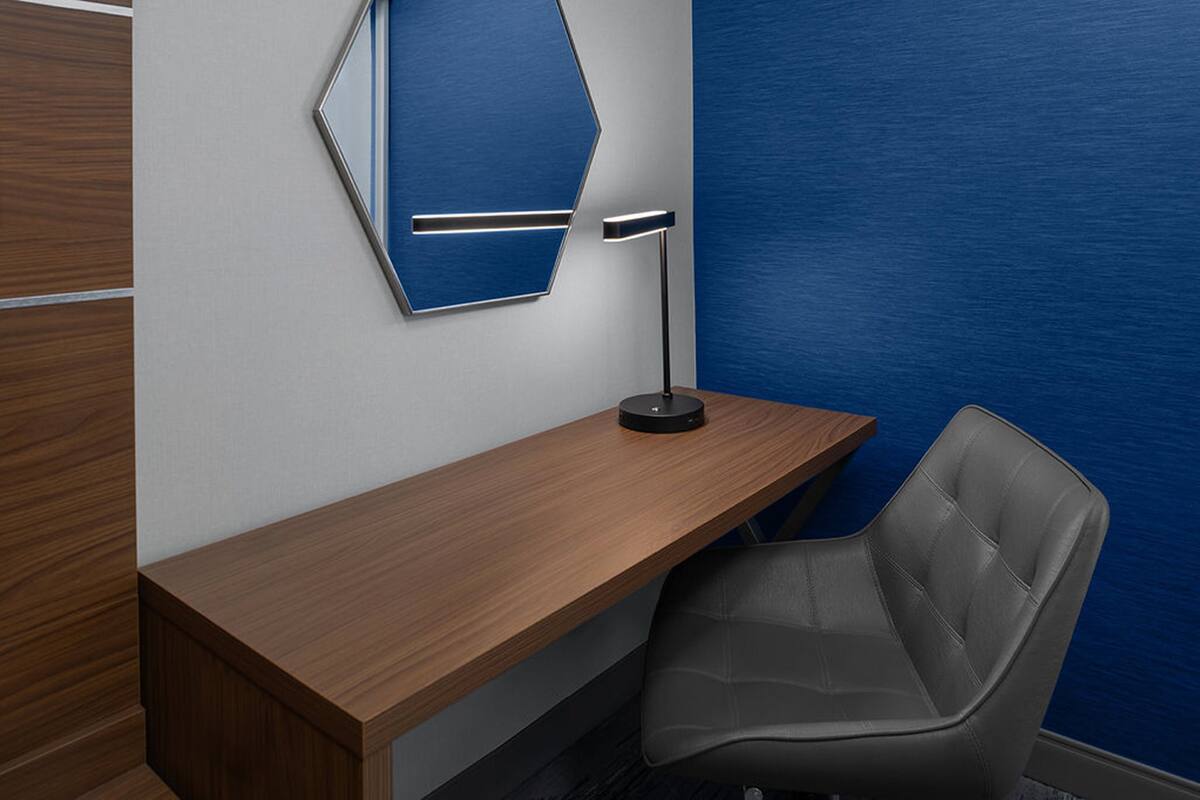 Un espace de bureau moderne avec un bureau en bois, une chaise de bureau grise, un mur d’accent bleu et un lampadaire.