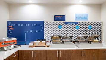 A breakfast buffet area with a blue directional sign, a pancake maker, and various food containers.