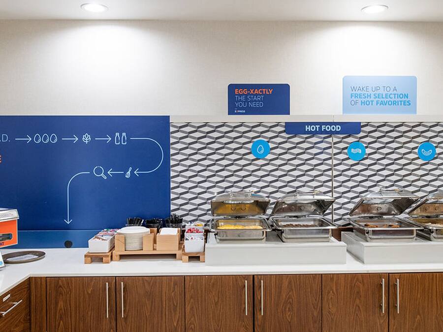 A breakfast buffet area with a blue directional sign, a pancake maker, and various food containers.