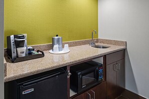 A compact kitchenette with a coffee maker, paper towels, a microwave, and a sink.