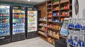 Una tienda de comestibles con dispensadores refrigerados para bebidas, estantes con aperitivos y un quiosco de pago.