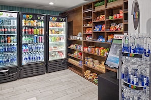 Una tienda de comestibles con dispensadores refrigerados para bebidas, estantes con aperitivos y un quiosco de pago.