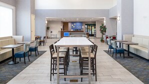Un amplio vestíbulo de hotel con zona de comedor central, espacios de estar y un mostrador de recepción.