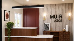 A reception desk with a wooden finish, a framed picture, and a wall-mounted sign that reads 'MUIR LODGE'. - Muir Lodge Motel (Martinez)