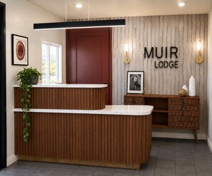 A reception desk with a wooden finish, a framed picture, and a wall-mounted sign that reads 'MUIR LODGE'. - Muir Lodge Motel (Martinez)