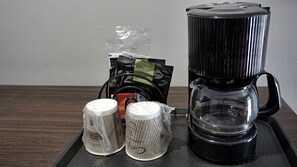 Uma cafeteira, dois objetos embalados e um saco de cápsulas de café numa bandeja.
