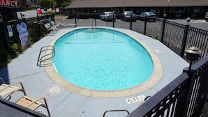 Una piscina con indicador de profundidad de 1.8 metros, rodeada por una cerca de metal negro, y un cartel que indica que está prohibido sumergirse.