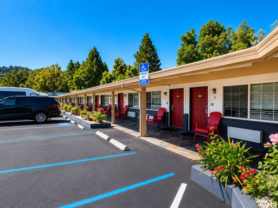 Ein Motel mit Parkplatz, roten Stühlen und einem blauen Parkplatzschild für Rollstuhlfahrer.