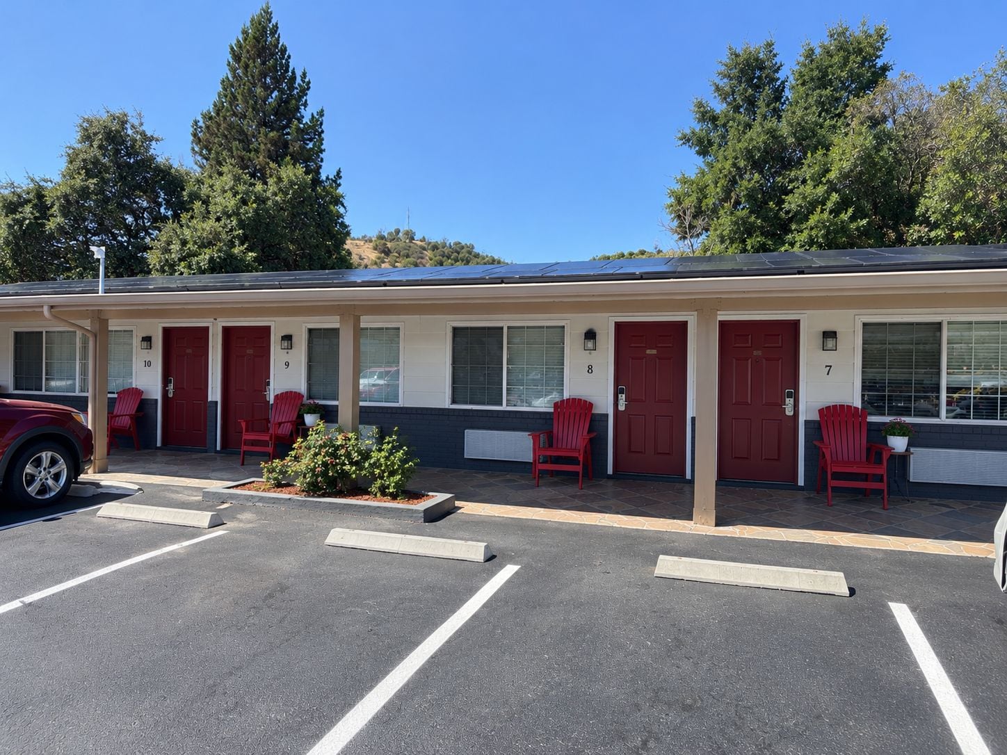Un motel con habitaciones numeradas, puertas rojas y un estacionamiento.